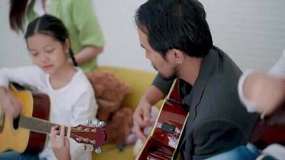 在音乐教室里一名男教师一边弹吉他一边给一起坐在黄色沙发上的7岁亚裔小学女孩提建议音乐教室乐器弦乐器