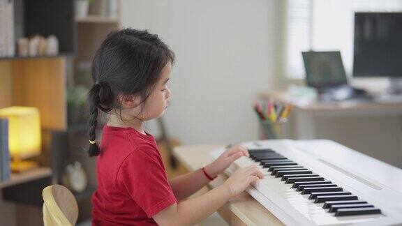 快乐的亚洲可爱小女孩微笑着在家里的客厅里学习在线钢琴音乐隔离期间儿童在家活动的想法音乐学习学习