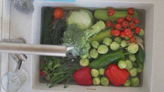 厨房水槽里的蔬菜正在清洗自来水浇在上面
