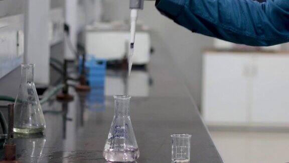 这是一位研究科学家的双手将一种无色的化学物质从微型吸管倒入一个锥形烧瓶中