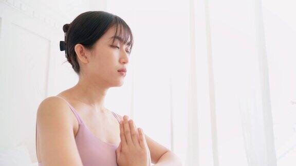 特写的运动美丽的亚洲妇女慢慢睁开她的眼睛同时在床上练习瑜伽作为地运动半莲花式合十礼冥想在家进行室内锻炼