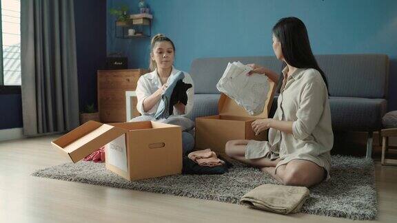 两个亚洲妇女把旧衣服放进纸板箱里她们要捐赠