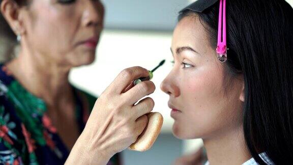亚洲女性化妆品用特殊的刷子在年轻女性的皮肤上涂粉