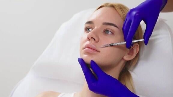 一位戴着医用手套的美容师正在用注射器慢慢地将透明质酸注射到一位年轻女子的嘴唇上丰唇手术注射美容