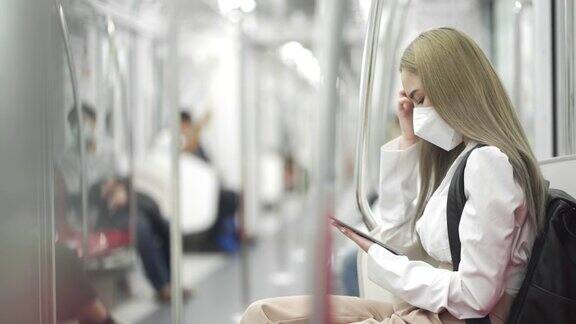 4K女商人戴着防护口罩坐在地铁上用数码平板电脑