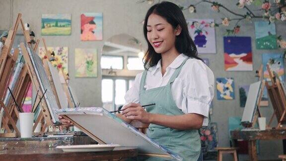 女子在画室里用油画颜料在画布上作画女艺术家在车间画画年轻的女艺术家在家里拿着调色板用画笔在画布上作画