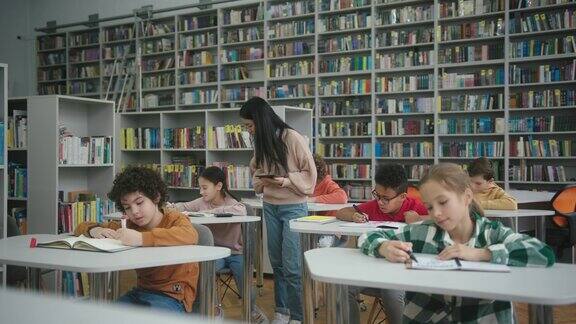 亚洲老师拿着平板看男孩在图书馆画画