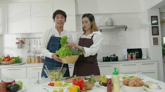 年轻的亚洲夫妇在厨房展示蔬菜和微笑