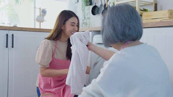 亚洲可爱的家庭做家务和家务在家里的厨房年轻的女儿帮助和支持年长的母亲把衣服放进洗衣机里洗客房清洁概念