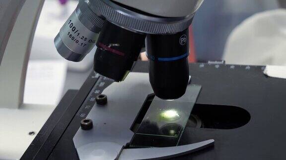 实验室助理一边在显微镜下检查载玻片上的样品一边把镜头调到放大率更高的位置在实验室用显微镜工作