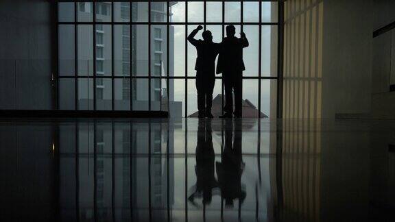 两个商人的剪影站在一个有大窗户的大办公室里
