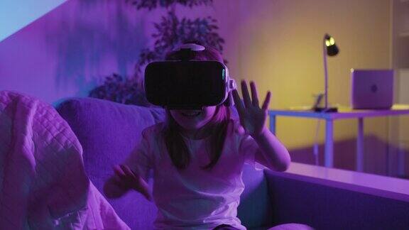 小女孩坐在黑暗房间的床上使用虚拟或增强现实眼镜