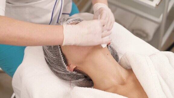 一个专业治疗师用白色餐巾清洁女性客户的脸和脖子的特写美容保健理念