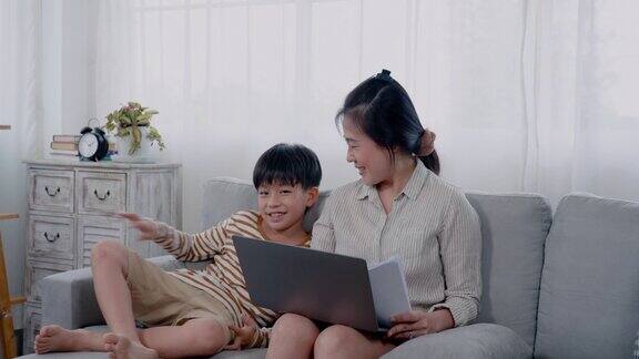 一个英俊的亚洲男孩跑到他的母亲身边坐下而他的母亲正在用笔记本电脑他的母亲转过身来亲切地看着她的儿子开心地笑了