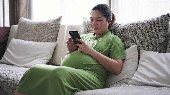 身着绿色套装的孕妇坐在家里客厅的沙发上使用手机
