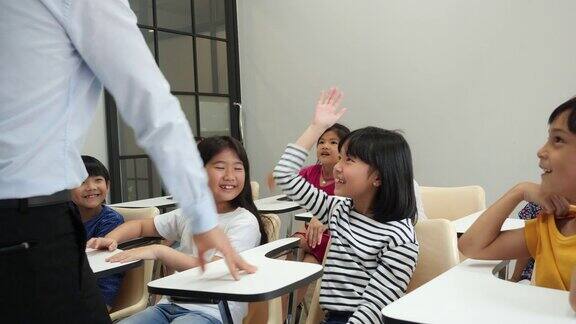 亚洲老师在学校的教室里教孩子们小男孩和小女孩一起举手接受评论教育理念、经验学习和技能发展