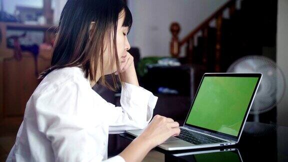 年轻女子在家里用绿色屏幕在笔记本电脑上工作