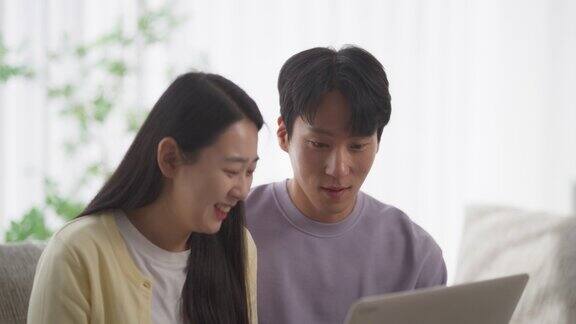 一对幸福的韩国夫妇在家里度过美好时光在舒适的公寓里营造和谐的氛围在笔记本电脑上观看韩剧