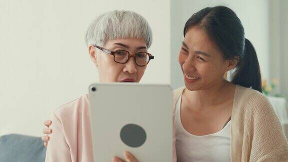 快乐的亚洲家庭年幼的女儿和年长的妈妈教年长的妈妈使用数字平板电脑在线视频电话朋友花时间在家里的周末
