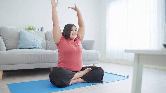 亚洲年轻的特大号女人在家里的客厅里做瑜伽练习吸引人的大码女孩锻炼遵循普拉提指导视频从在线教练在电视上在家里减肥