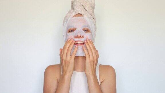 满意的妇女在面部皮肤上使用化妆品白色纺织品面膜使用组织织物纺织品面膜进行美容治疗隔离在白色背景上