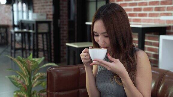 美丽的亚洲女人舒适地坐在café的咖啡她啜了一口闻到了咖啡的香味