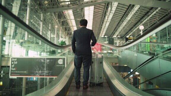 商人站在机场自动扶梯上的后视图