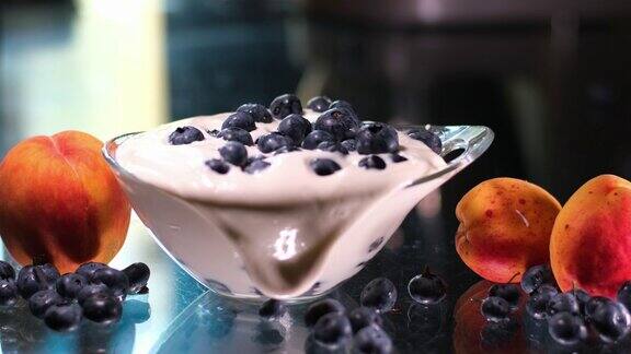 把蓝莓和浓稠的酸奶油倒在玻璃盘里旁边是桃子和杏蓝莓酸奶美味的液体白酸奶油和蓝莓的质地奶油乳制品