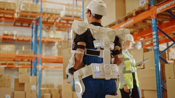 高科技未来仓库:工人穿着先进的全身动力外骨骼与沉重的纸板箱行走Exosuit增强了人类的力量跟随低角度多莉后视图