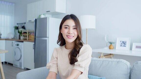 亚洲美女肖像坐在家里客厅的沙发上有魅力的年轻女性感到快乐和放松享受清晨周末活动生活方式在家里微笑看着相机