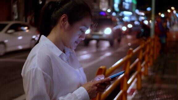 亚洲微笑女性在夜晚使用智能手机女人在城市里边走边打电话女性独自在街上行走晚上在路上用智能手机和朋友交流生活方式