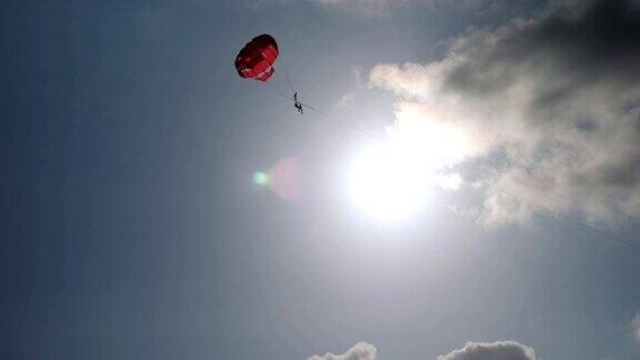 在晴朗的蓝天下游客在红色的降落伞上滑翔