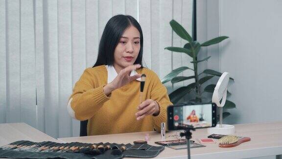 一位年轻的亚洲女性在家里用手机相机拍摄了一段关于化妆品的视频并在她的博客上写了关于美容产品的视频