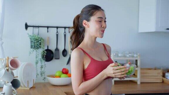 亚洲迷人的运动女子拿着沙拉碗和吃蔬菜漂亮的运动女孩穿着运动服在家里享受运动后吃干净的蔬菜的健康饮食和健康食品