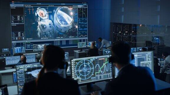 任务控制中心的一群人在一个大屏幕上与空间站上的宇航员成功建立视频连接飞行控制科学家坐在电脑显示器前