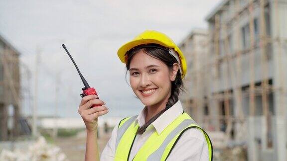 亚洲工头在现场用对讲机讨论建设工作的肖像同时看着房屋建设村发展项目侧面的看法与感到自豪的工作积极的情绪与微笑