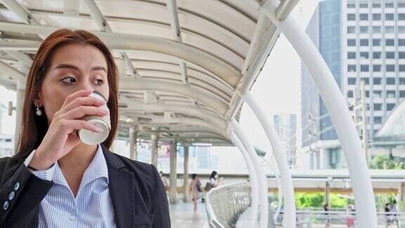 亚洲年轻女商人一边喝咖啡一边走在城市里在工作日休息和放松