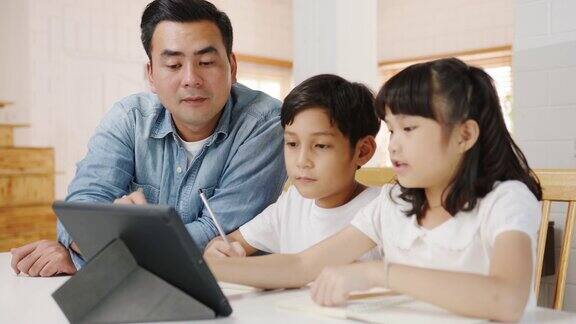 快乐亚洲家庭家庭教育爸爸在家里的客厅教孩子使用数码平板电脑