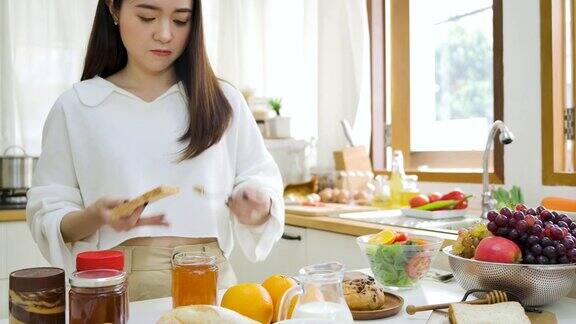 快乐的亚洲妇女在厨房的面包上涂果酱健康的饮食和健康