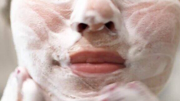 一位年轻女子正在洗脸用泡沫洗面奶洗脸日常面部护肤程序前视图