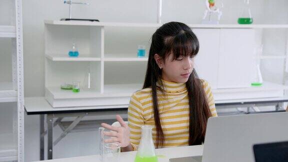 可爱的亚洲女学生在试管里科学地实验混合颜色在学校实验室里学习实验女孩坐在笔记本电脑前在上课时间记录实验数据