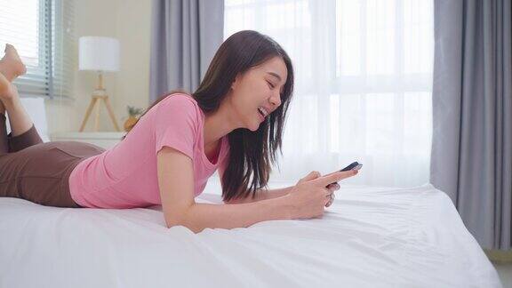 亚洲有魅力的女人早上在家的床上用手机聊天快乐休闲美丽的女性躺在卧室享受假期周末使用智能手机与技术在家里沟通