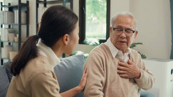 特写年轻的亚洲女性看护者握着老男性的手在家里的沙发上照顾老年病人