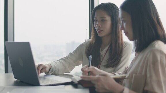 两个年轻貌美的亚洲女商人坐在办公室里在会议室里使用笔记本电脑