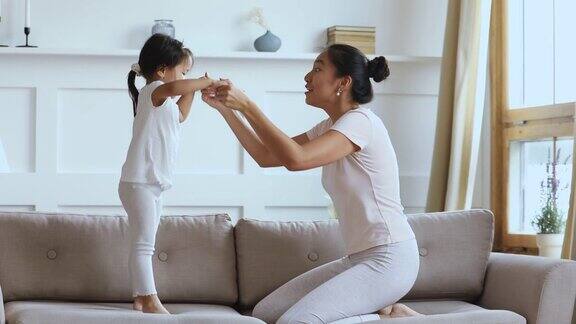 可爱的亚洲小女孩跳上沙发和妈妈玩