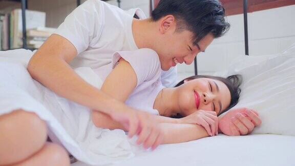 亚洲丈夫在卧室的床上躺着睡觉时亲吻妻子美丽的新婚夫妇穿着睡衣感觉幸福和放松在清晨一起在家里度过闲暇时间