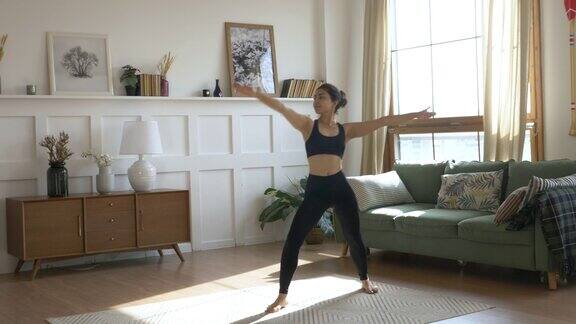 年轻的印度女人做冥想锻炼伸展运动瑜伽衣服黑色打底裤和筒形上衣在家里明亮的房间