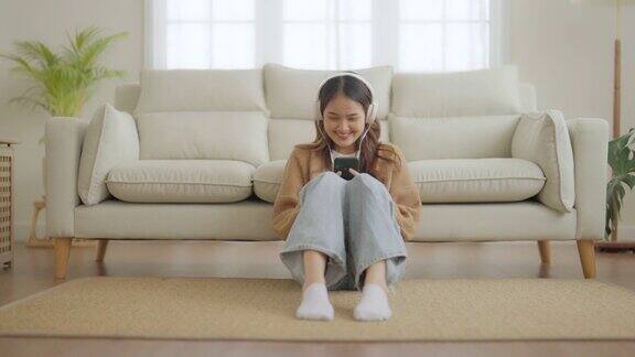 快乐的年轻亚洲女性在家放松女人坐在沙发上微笑手里拿着手机女孩给朋友打视频电话