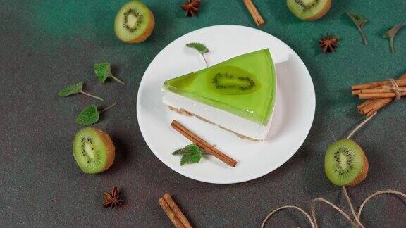 近距离自制奶酪蛋糕与猕猴桃在一个白色盘子上的绿色背景装饰以猕猴桃片肉桂棒和薄荷叶