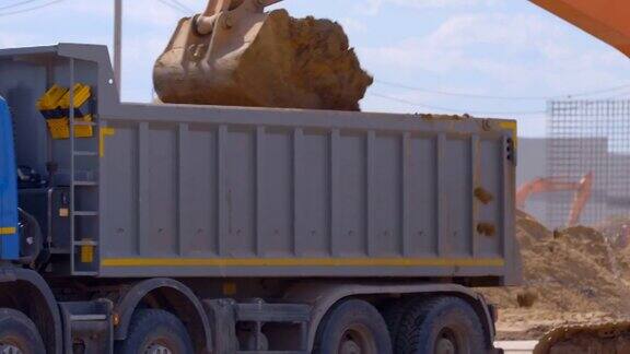 一辆卡车在尘土飞扬的路上倒车准备用挖掘机装土
